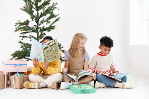 Three children read Honest History Magazine next to a Christmas tree and presents